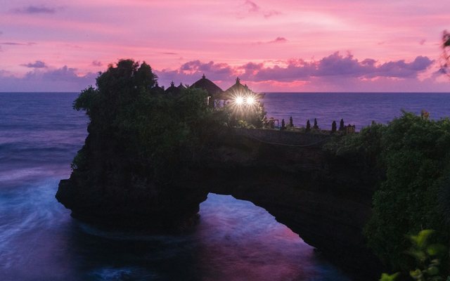 Temple on a rock arch over the ocean at sunset